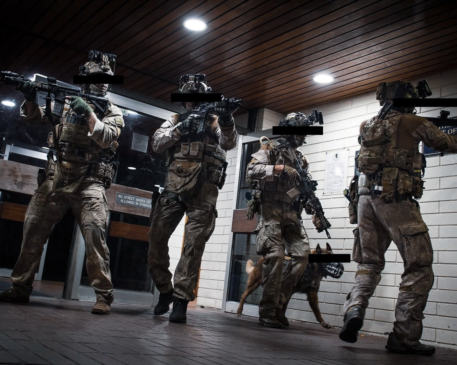 Four NZ SAS soldiers in tactical gear walking through a building interior with a working K9 in a muzzle.