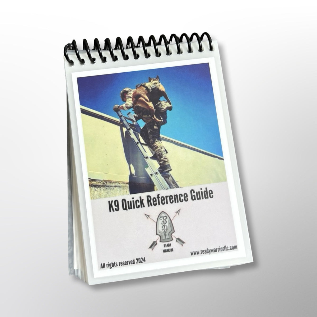 Front cover of the Ready Warrior K9 Quick Reference Guide, a spiral-bound, laminated pocket guide, showing a handler carrying a K9 up a ladder